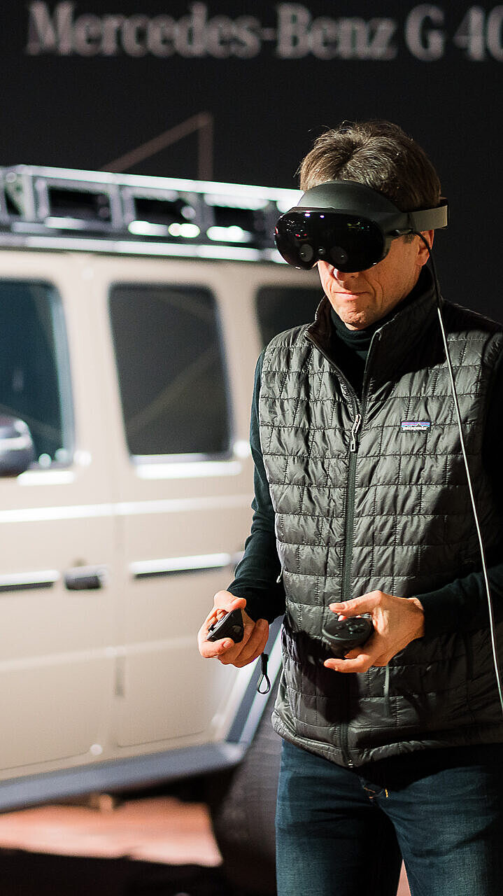 Participant using a VR headset to explore a Mercedes-Benz vehicle in a virtual environment.