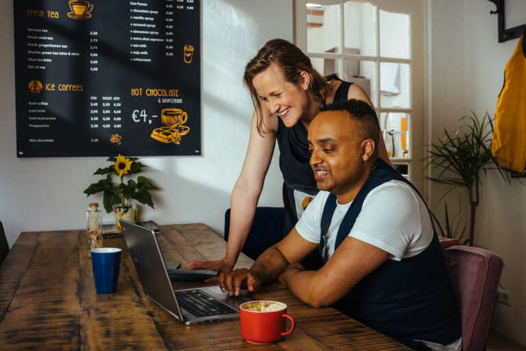 Two colleagues discussing something on a laptop in a café.